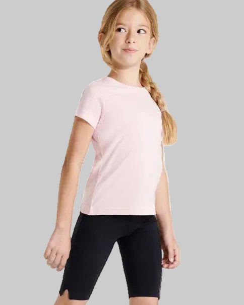 A young girl with a blonde braid wearing a light pink short-sleeve t-shirt and black bike shorts, standing against a plain light gray studio background.