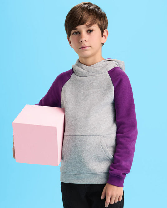 Child wearing a gray and purple hoodie holding a pink box against a blue background