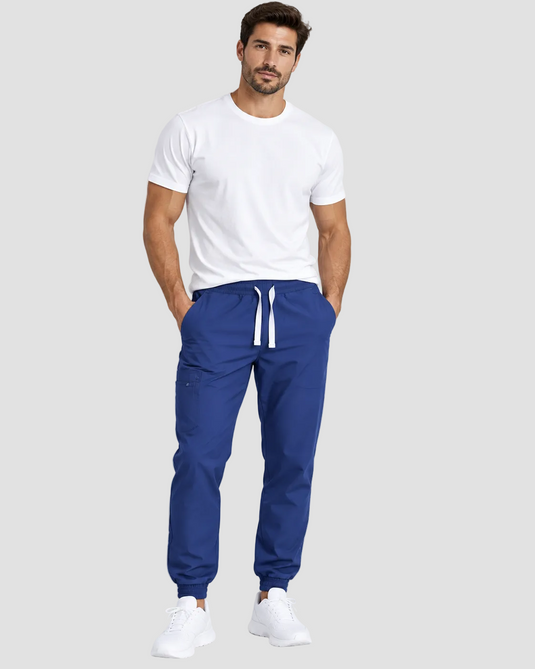 A man modeling a white crewneck t-shirt and royal blue jogger pants with white drawstrings, paired with white sneakers, against a light gray studio background.